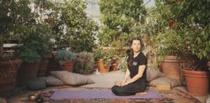 Sara Serroni, insegnante di Yoga Vinyasa, seduta in meditazione su un tappetino in un giardino con piante